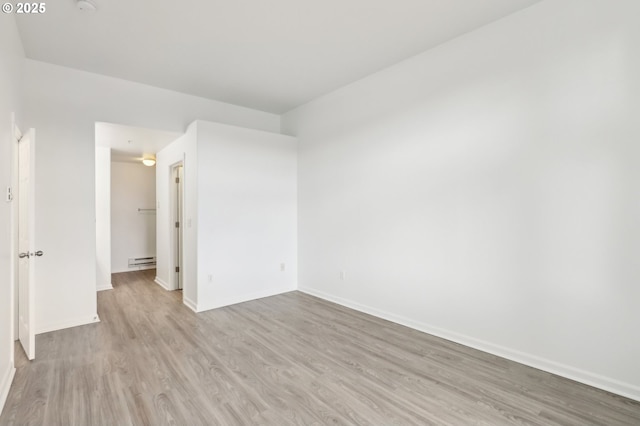 empty room with baseboards, a baseboard radiator, and wood finished floors