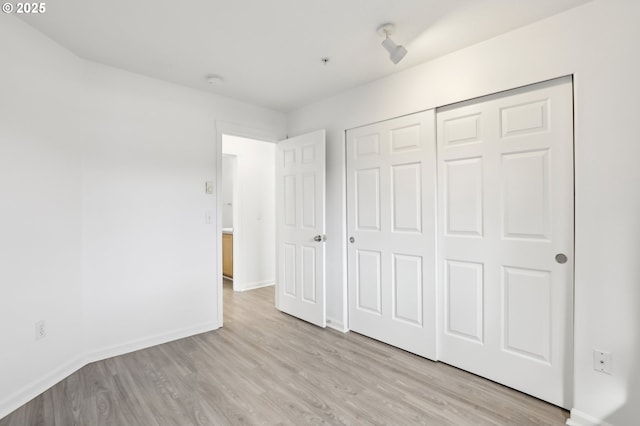 unfurnished bedroom with light wood-type flooring, baseboards, and a closet