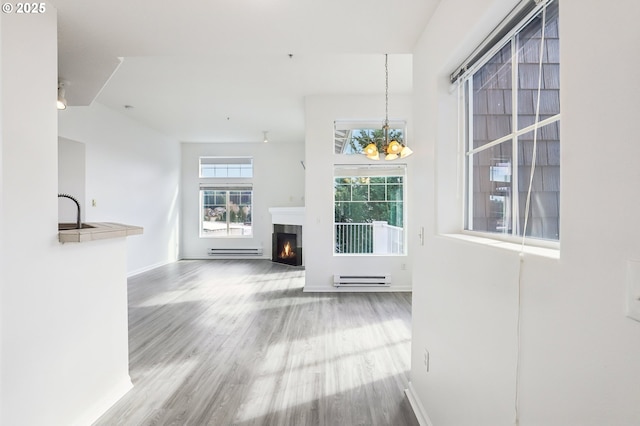 unfurnished living room featuring wood finished floors, baseboards, a baseboard heating unit, and a notable chandelier