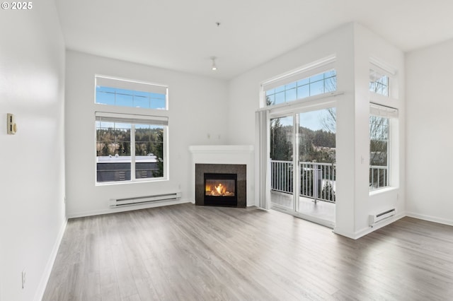 unfurnished living room featuring plenty of natural light, a glass covered fireplace, wood finished floors, and baseboard heating
