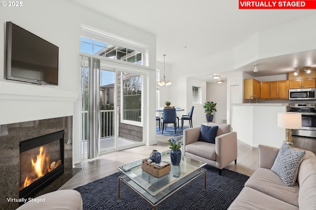 living area with a glass covered fireplace, wood finished floors, and a notable chandelier