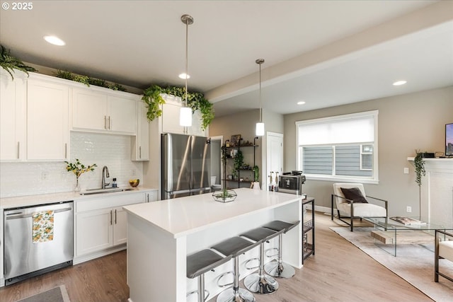kitchen with stainless steel appliances, a sink, light wood-style floors, decorative backsplash, and light countertops