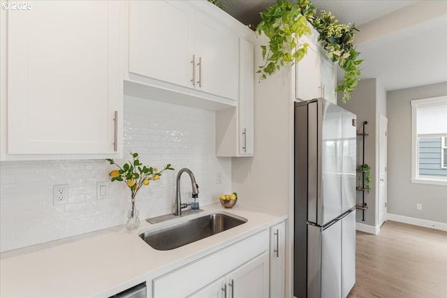 kitchen featuring freestanding refrigerator, a sink, decorative backsplash, white cabinets, and light countertops