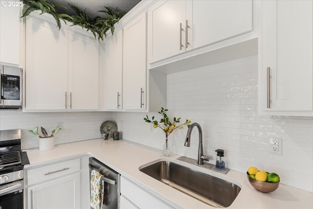 kitchen with a sink, appliances with stainless steel finishes, backsplash, and white cabinetry