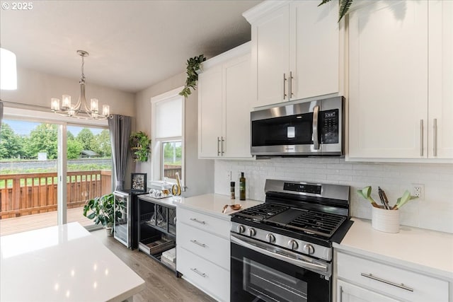 kitchen with appliances with stainless steel finishes, backsplash, a chandelier, light countertops, and white cabinets