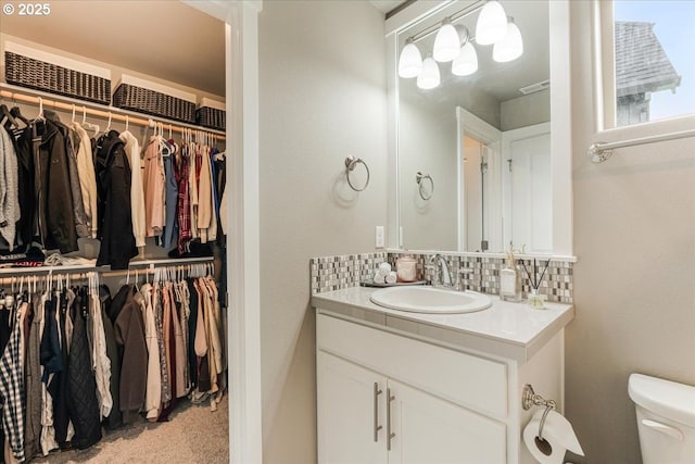 bathroom featuring toilet, vanity, tasteful backsplash, and a spacious closet