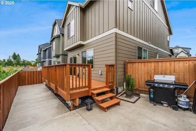 back of house with board and batten siding, fence, a wooden deck, and a patio area