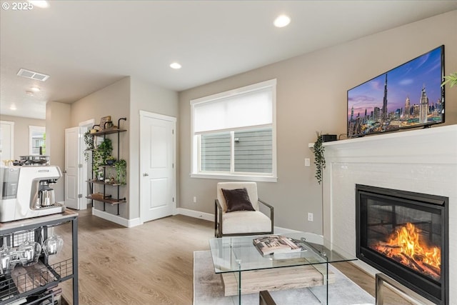 living room with wood finished floors, a glass covered fireplace, baseboards, and recessed lighting