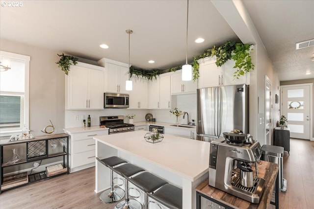kitchen featuring stainless steel appliances, a sink, tasteful backsplash, light countertops, and white cabinetry
