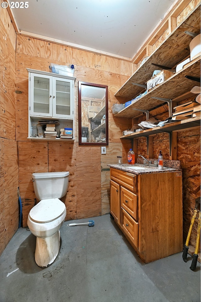bathroom with wooden walls, vanity, unfinished concrete floors, and toilet
