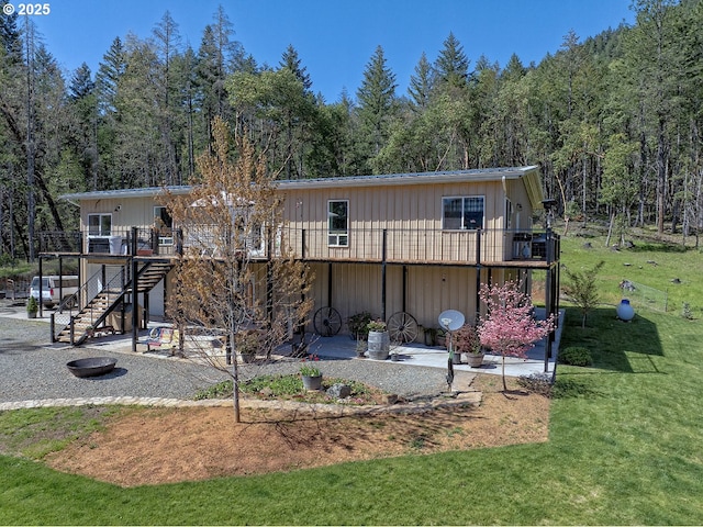 back of house featuring a lawn, a view of trees, a deck, and stairs