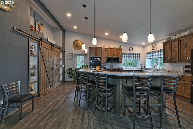 kitchen featuring a barn door, oven, a breakfast bar, stainless steel microwave, and dark wood-style floors