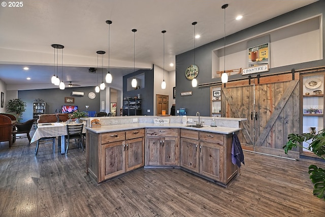 kitchen featuring ceiling fan, dark wood-type flooring, a barn door, decorative light fixtures, and a center island with sink