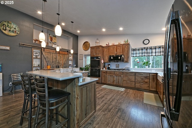 kitchen featuring black appliances, dark wood-type flooring, a center island with sink, and light countertops