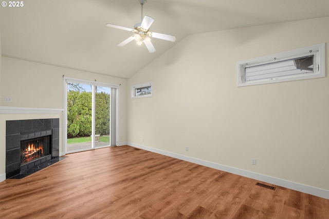 unfurnished living room with ceiling fan, wood-type flooring, a tiled fireplace, and vaulted ceiling