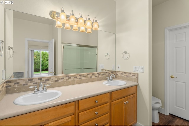 bathroom with toilet, hardwood / wood-style floors, walk in shower, vanity, and backsplash