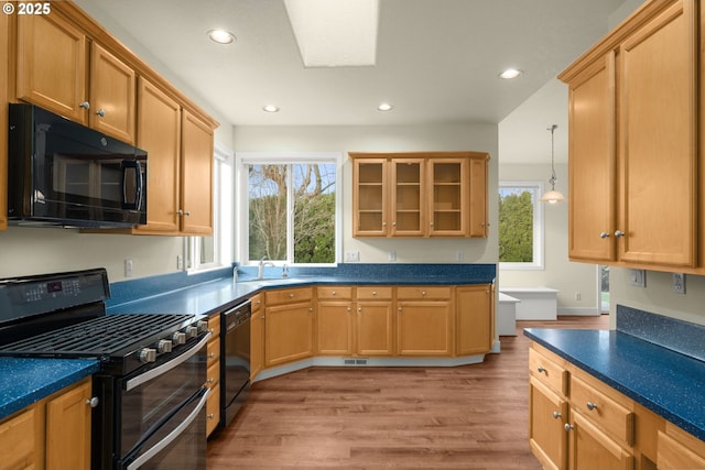 kitchen with pendant lighting, black appliances, a healthy amount of sunlight, and light hardwood / wood-style flooring