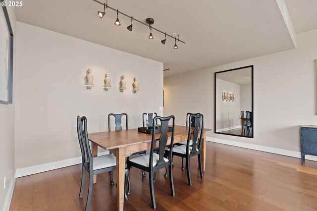 dining area with wood finished floors, baseboards, and rail lighting