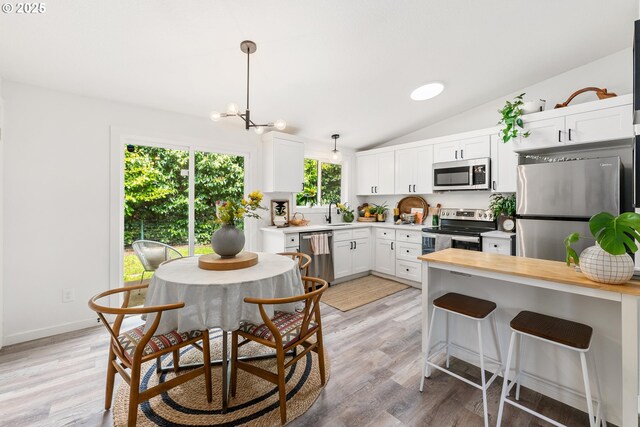 kitchen with appliances with stainless steel finishes, white cabinets, lofted ceiling, hanging light fixtures, and light wood-style flooring