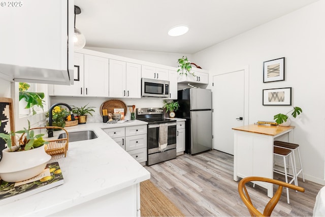 kitchen with appliances with stainless steel finishes, a sink, vaulted ceiling, light wood-type flooring, and white cabinetry