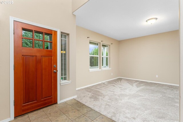 foyer entrance featuring light carpet, light tile patterned floors, and baseboards