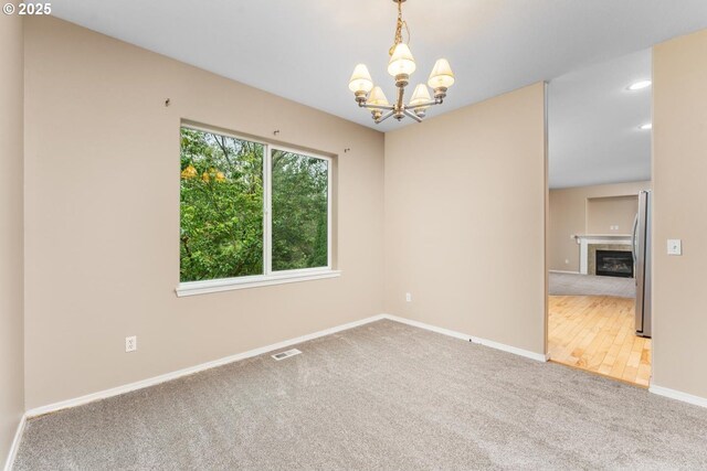 carpeted spare room with a chandelier, a tile fireplace, recessed lighting, visible vents, and baseboards