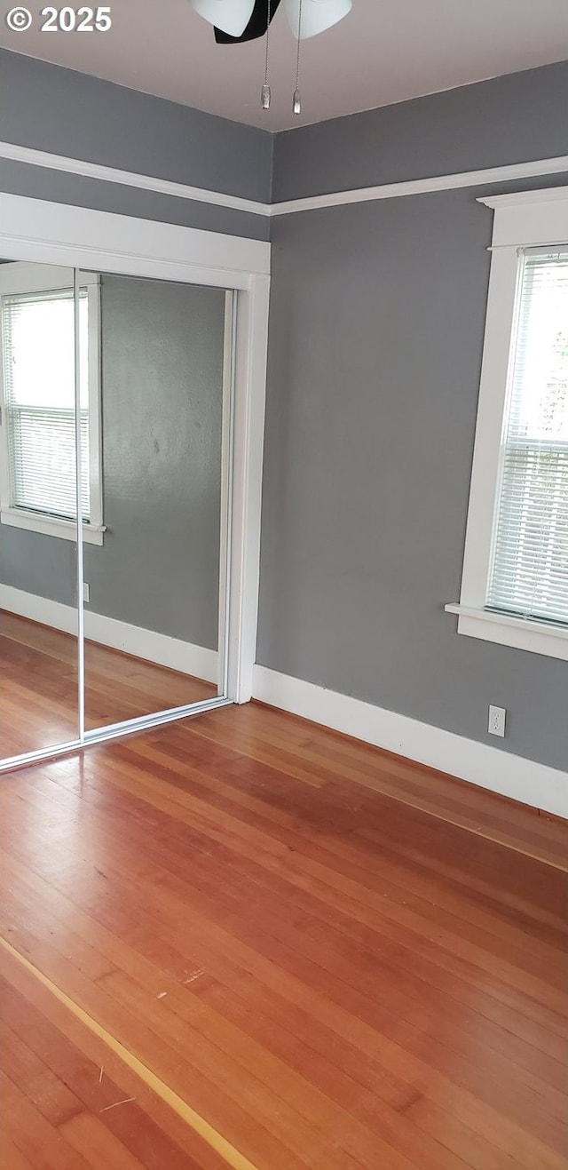 unfurnished bedroom featuring wood finished floors, baseboards, a closet, and a ceiling fan