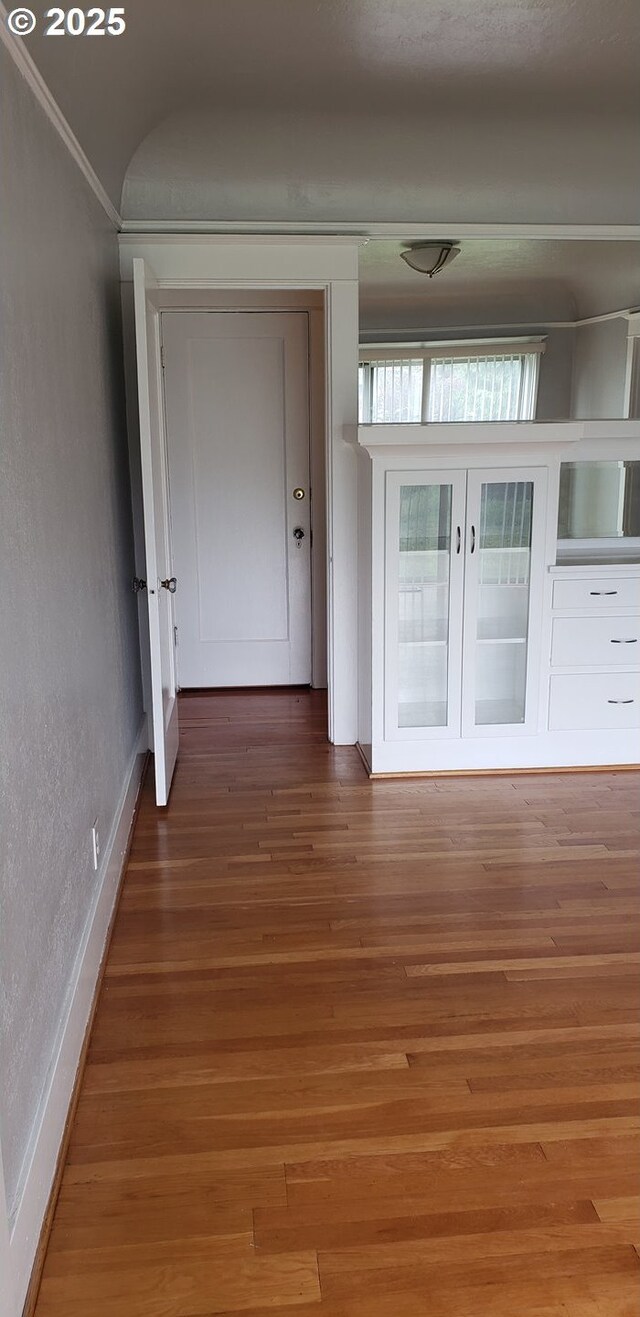 hallway with ornamental molding, wood finished floors, a textured wall, and baseboards