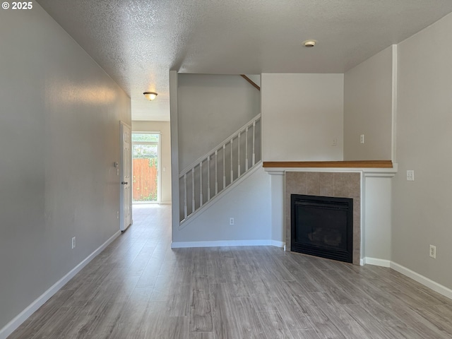 6668 SE 72nd Ave, Portland, OR 97206 - unfurnished living room with wood finished floors, a textured ceiling, stairway, a tile fireplace, and baseboards