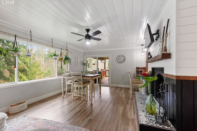 dining area featuring crown molding, a fireplace with raised hearth, wood ceiling, wood finished floors, and baseboards