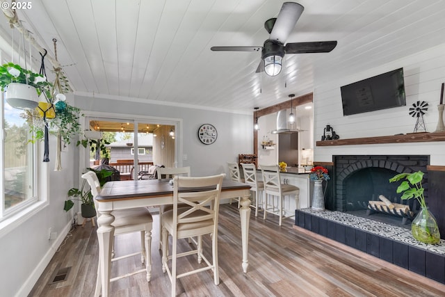 dining space with a fireplace with raised hearth, wood finished floors, wood ceiling, and baseboards