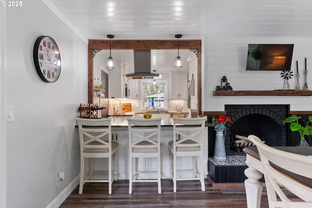 kitchen featuring baseboards, a breakfast bar area, dark wood-type flooring, island exhaust hood, and backsplash