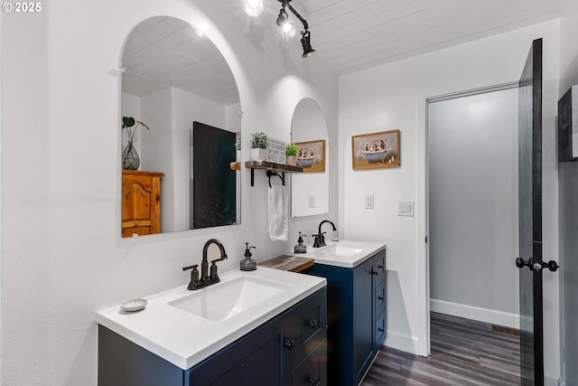 full bath featuring baseboards, two vanities, a sink, and wood finished floors