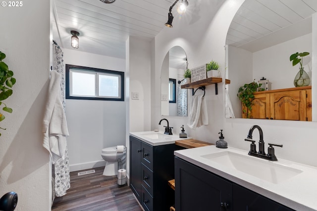 bathroom with toilet, two vanities, a sink, and wood finished floors