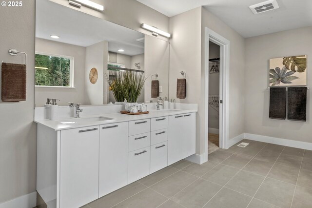 full bath with double vanity, a walk in closet, tile patterned flooring, baseboards, and a shower