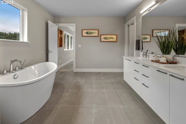 bathroom featuring a freestanding bath, tile patterned floors, double vanity, and baseboards