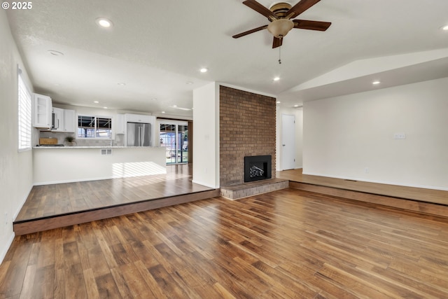 unfurnished living room featuring ceiling fan, lofted ceiling, a fireplace, and light wood-type flooring