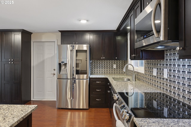 kitchen featuring stainless steel appliances, a sink, dark wood-type flooring, and light stone countertops