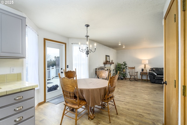 dining space featuring light wood finished floors, a textured ceiling, and a notable chandelier