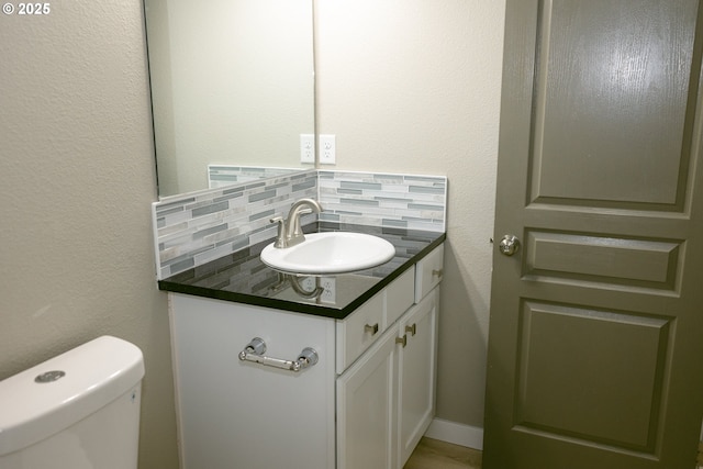 half bathroom featuring a textured wall, toilet, backsplash, and vanity