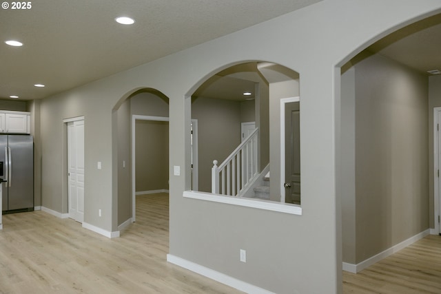 hall featuring light wood finished floors, stairs, baseboards, and recessed lighting