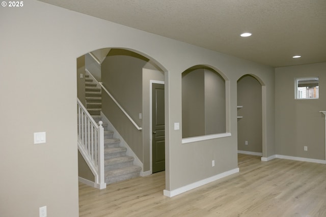 empty room featuring a textured ceiling, recessed lighting, wood finished floors, baseboards, and stairway