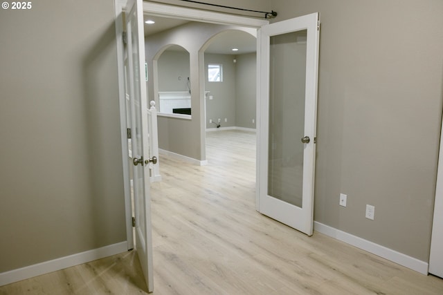 hallway with arched walkways, french doors, baseboards, and light wood-style floors