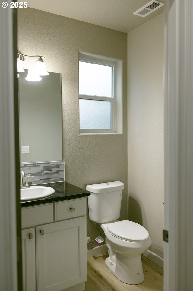 bathroom featuring visible vents, toilet, vanity, wood finished floors, and baseboards