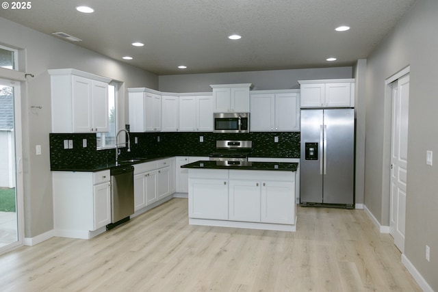 kitchen with light wood finished floors, appliances with stainless steel finishes, white cabinets, a sink, and a kitchen island