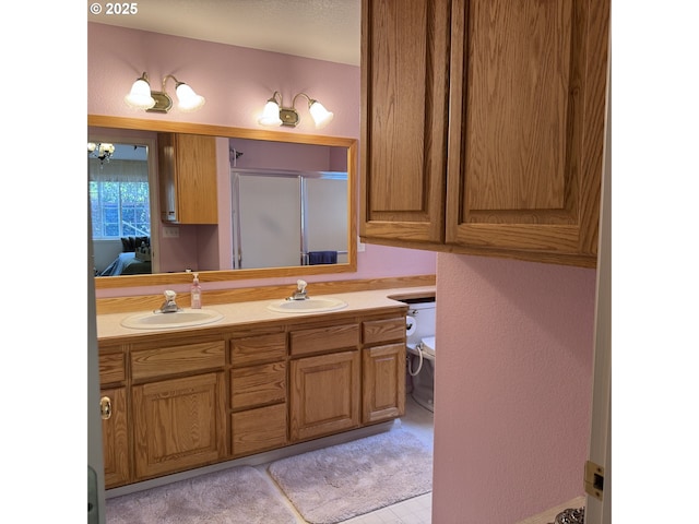 bathroom featuring a shower with door, double vanity, toilet, and a sink