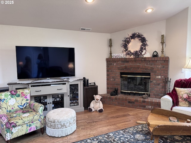 living room featuring a brick fireplace, recessed lighting, wood finished floors, and visible vents