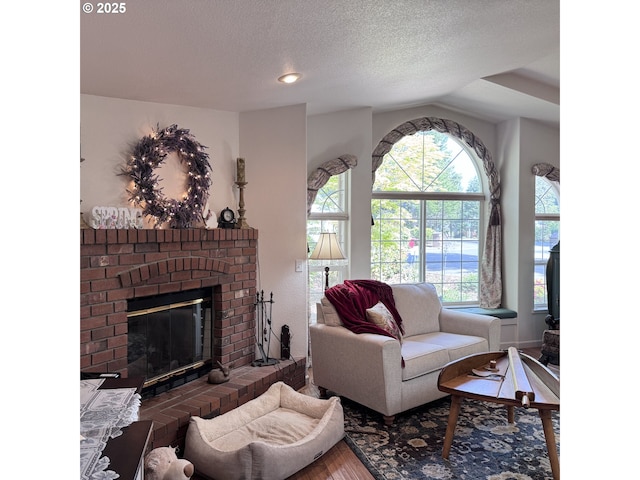 living area with a brick fireplace, a textured ceiling, and wood finished floors