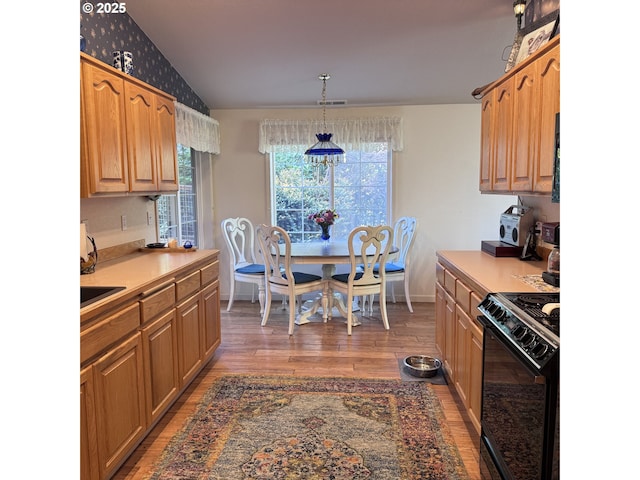 kitchen featuring lofted ceiling, black gas stove, baseboards, light wood-style flooring, and decorative light fixtures