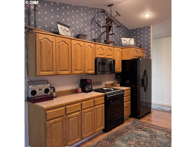 kitchen featuring light wood-style flooring, baseboards, wallpapered walls, vaulted ceiling, and black appliances